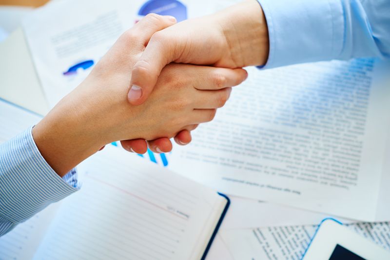 Close-up of female and male handshaking over workplace with business documents
